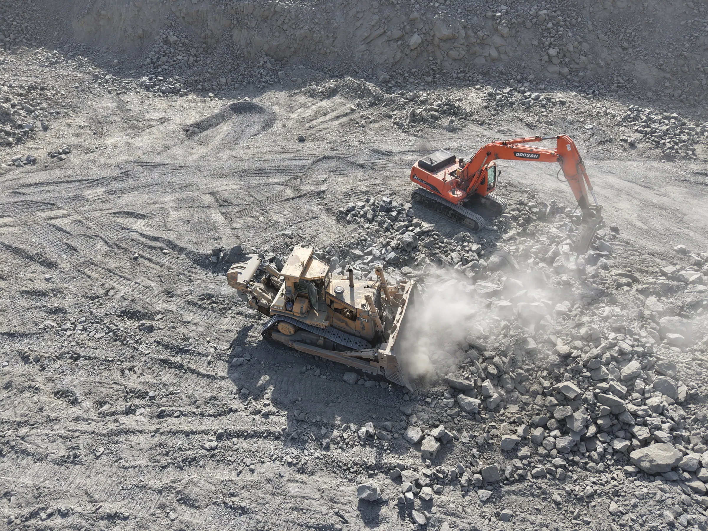Excavator and bulldozer working broken rock on the quarry floor, seen from above