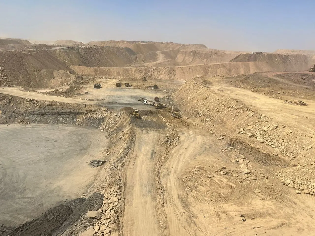 Elevated view across pale open-pit benches, haul roads and the working fleet