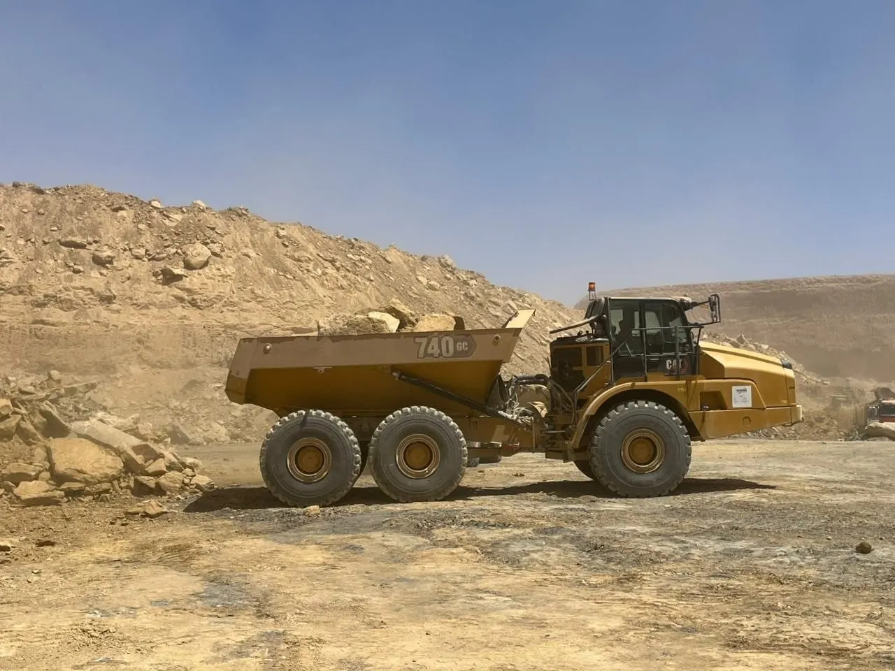 Articulated hauler carrying broken rock across the pit floor beneath a spoil slope